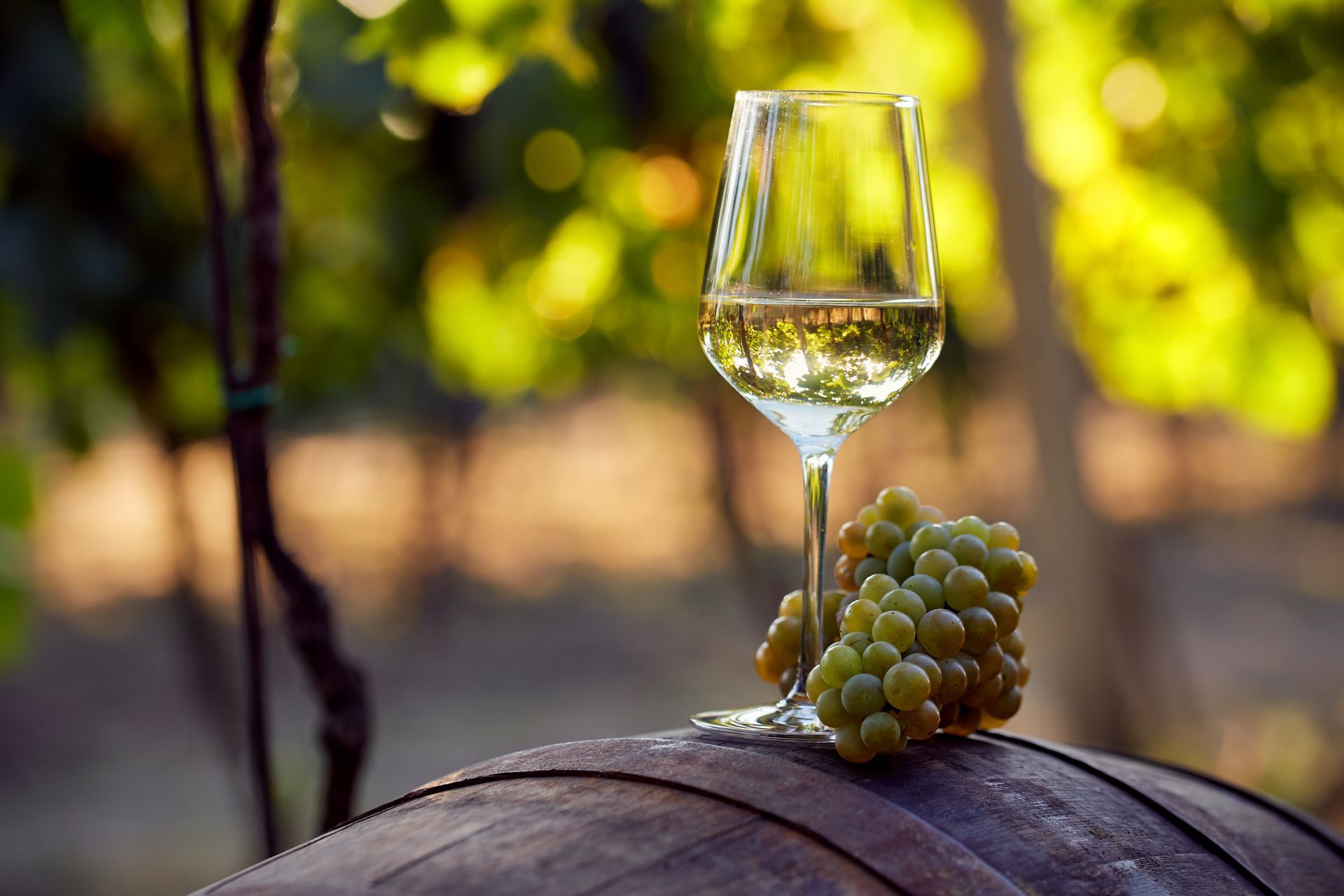 A glass of wine is sitting on top of a wooden barrel next to a bunch of grapes.