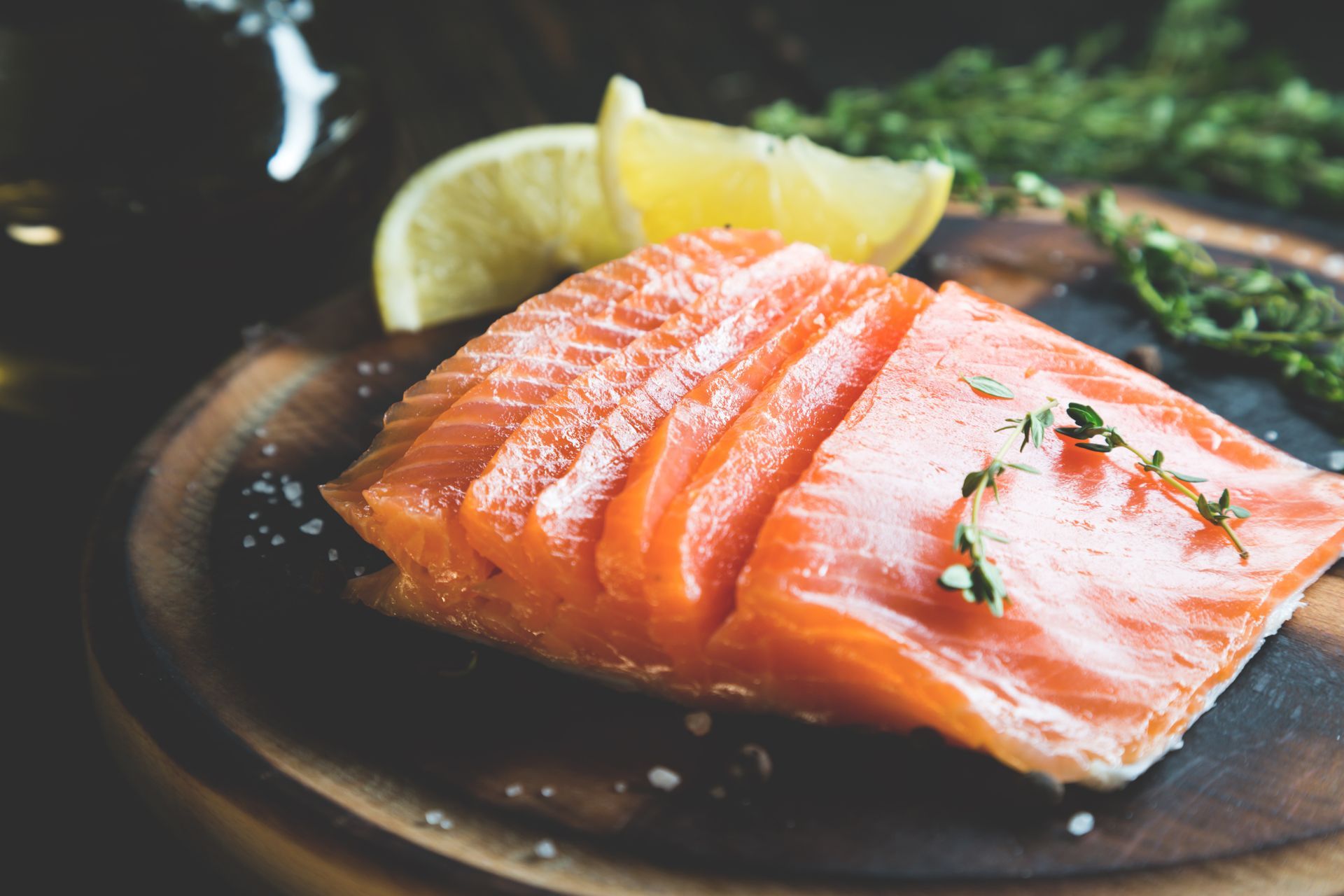A piece of salmon on a wooden cutting board with lemon slices.