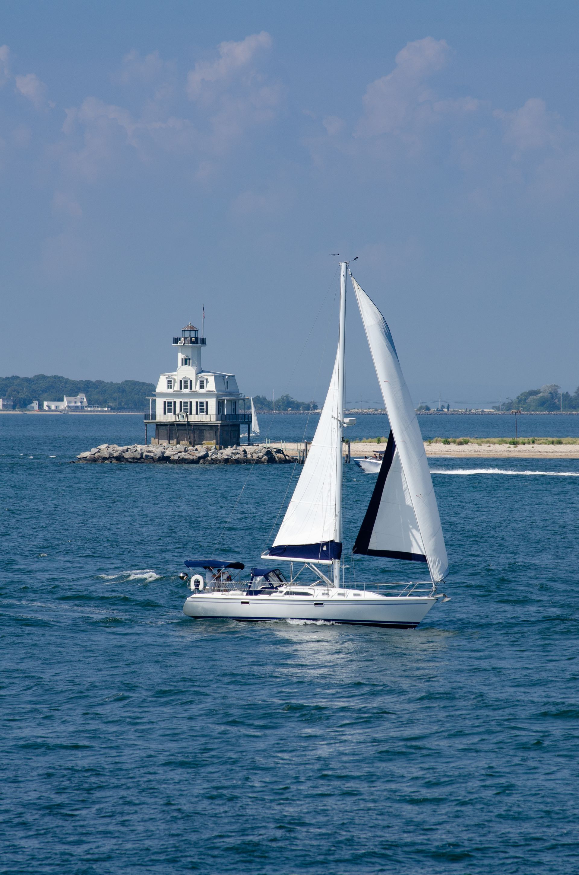 A sailboat is floating on top of a body of water with a lighthouse in the background.