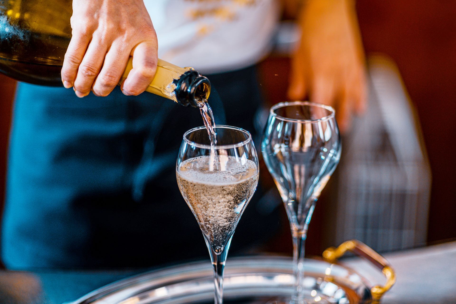 A person is pouring champagne into two glasses on a tray.