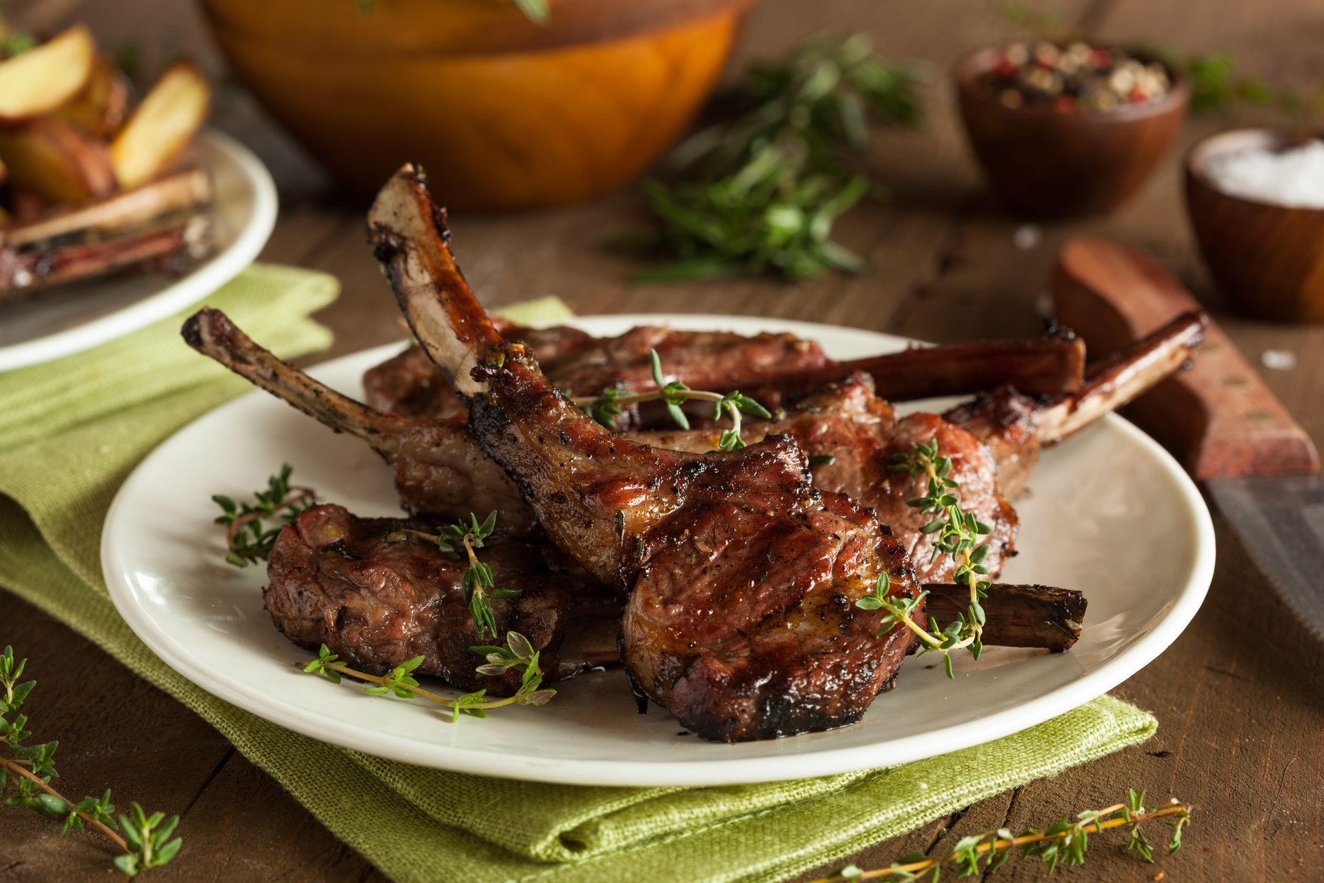 A white plate topped with lamb chops and potatoes on a wooden table.