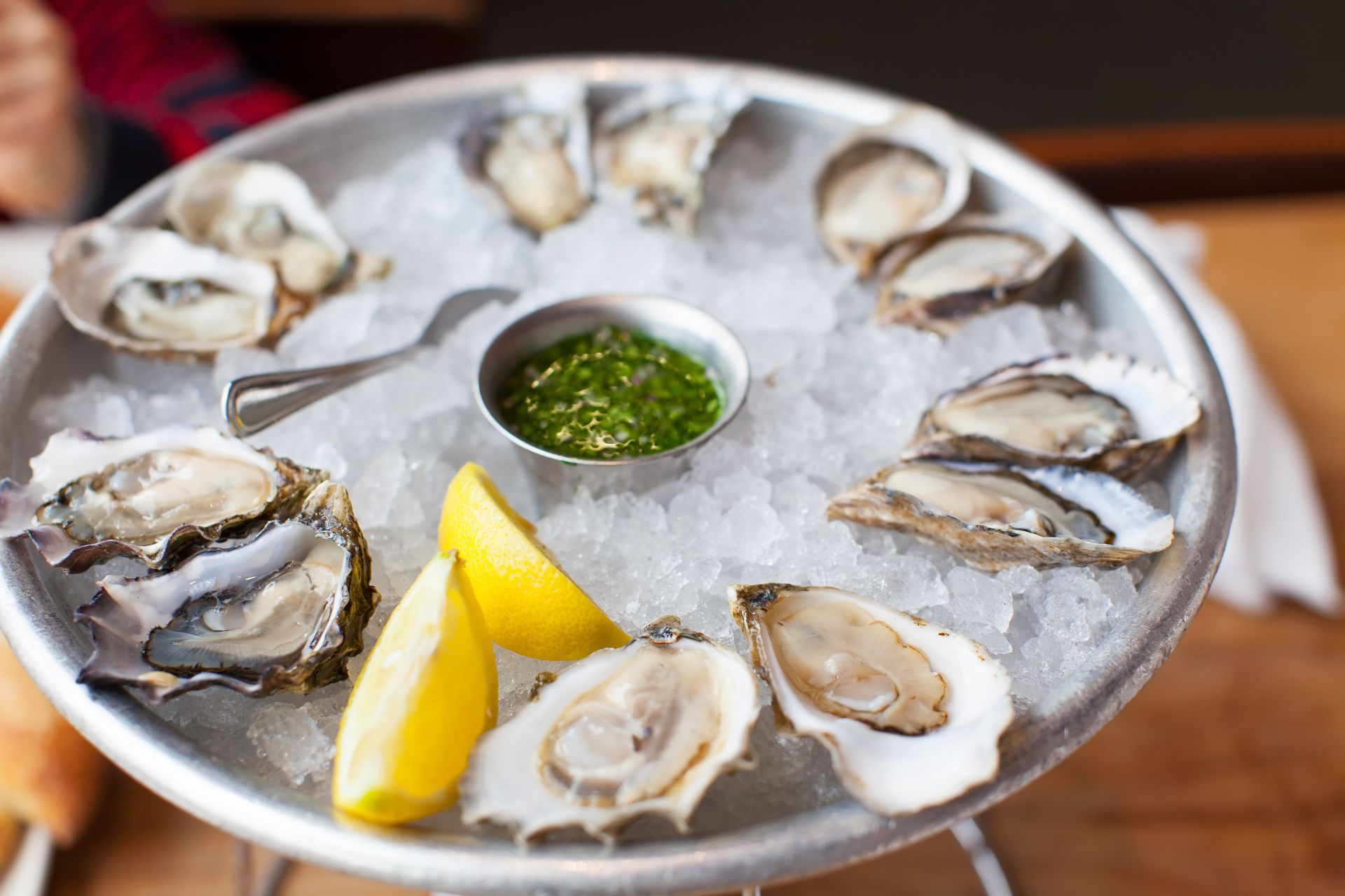 A tray of oysters on ice with lemon slices on a table.