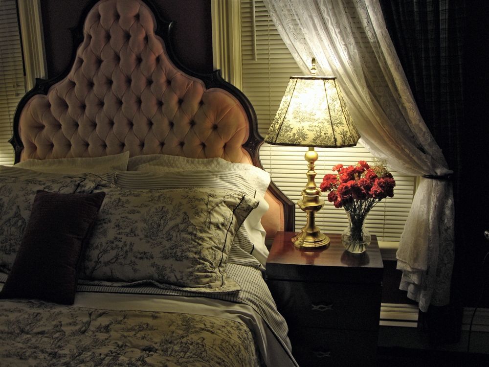 A bedroom with a bed a lamp and a vase of flowers