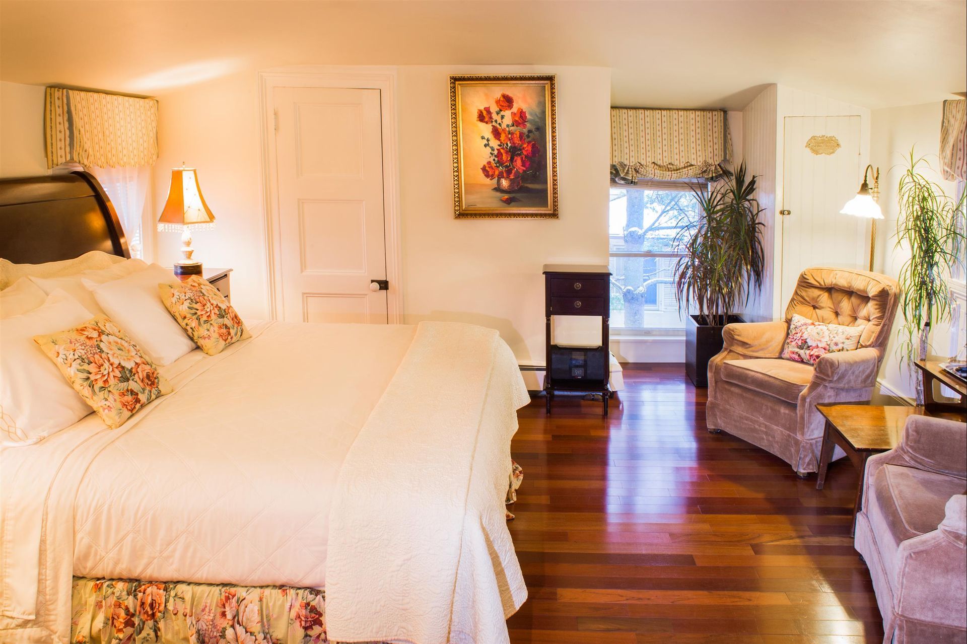 A bedroom with a large bed , chairs , lamps and a painting on the wall.