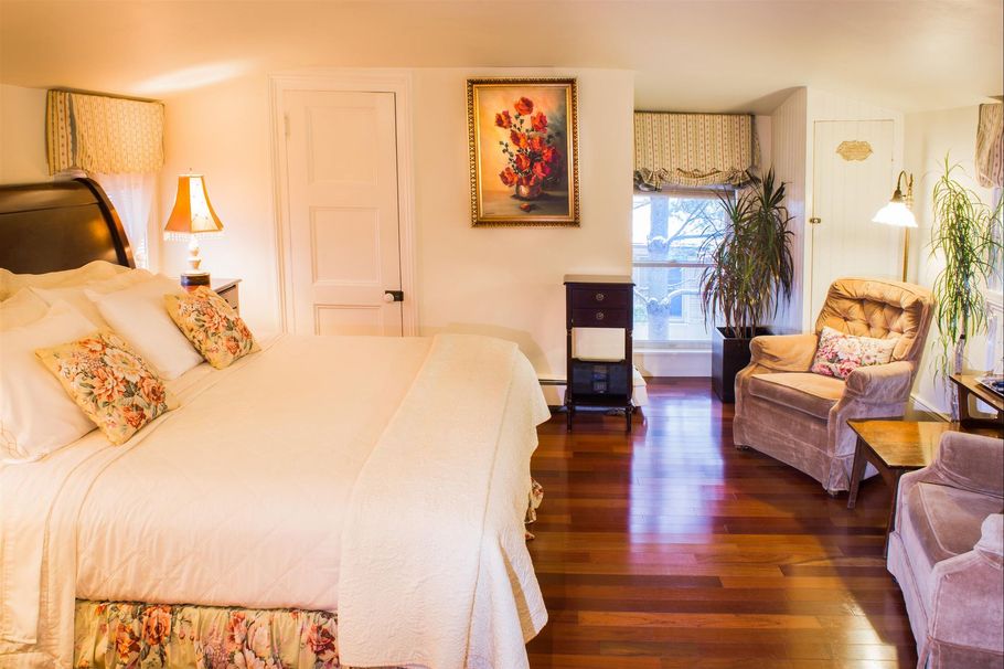 A bedroom with a large bed , chairs , lamps and a painting on the wall.