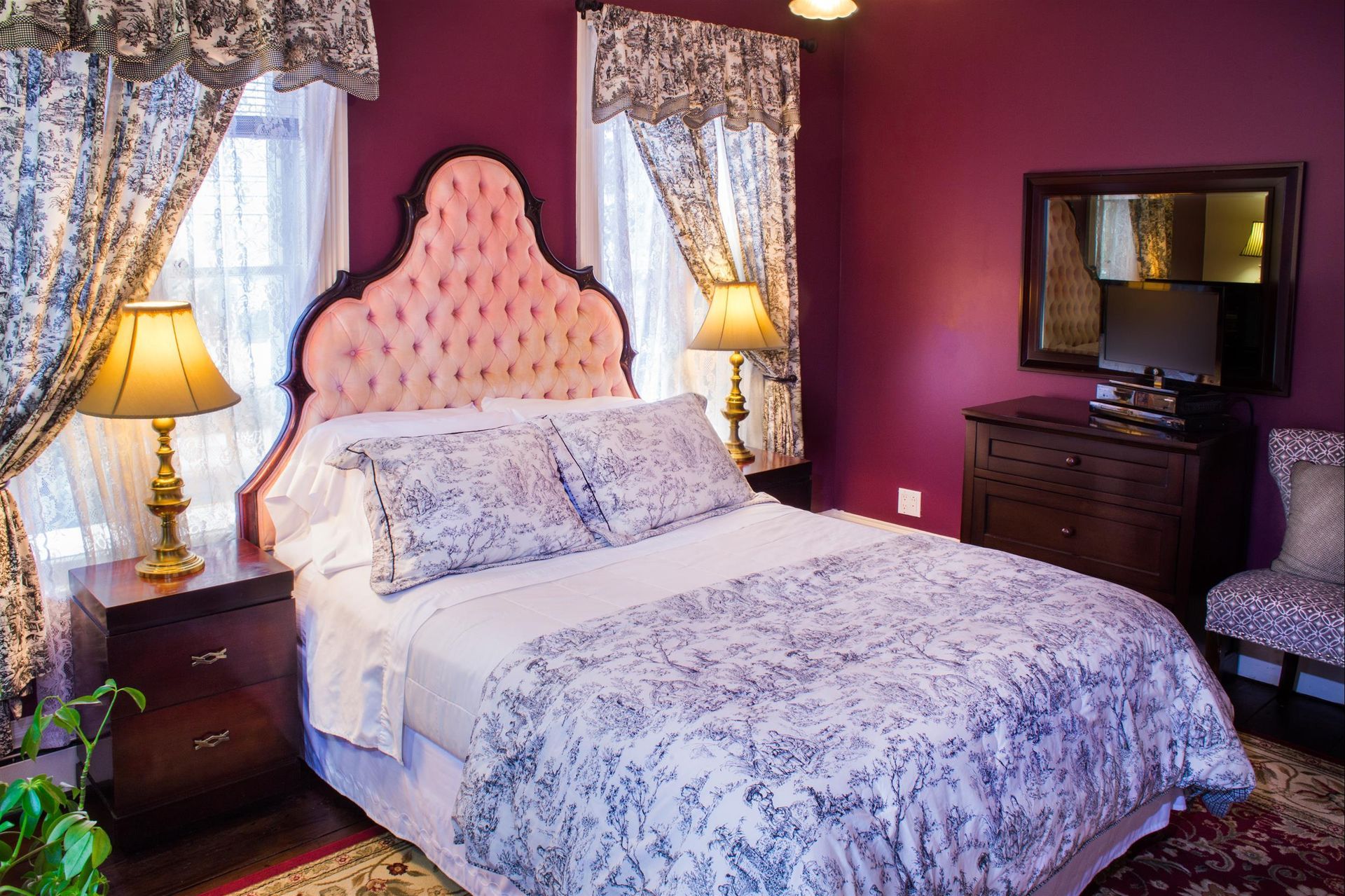 A bedroom with purple walls , a bed , two lamps , a chair and a mirror.