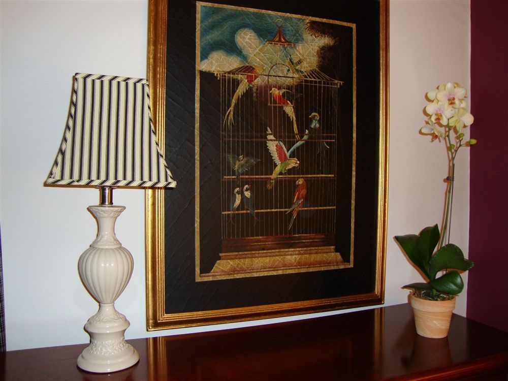 A lamp is on a table next to a picture of birds in a cage