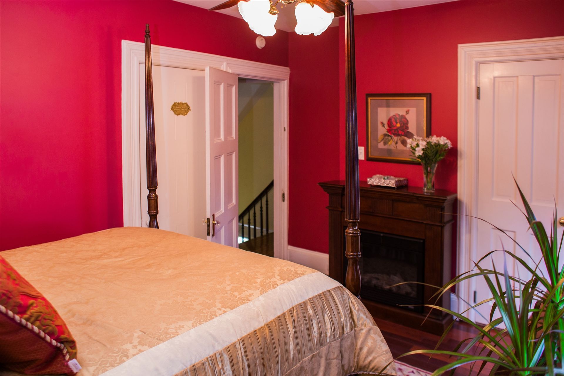 A bedroom with red walls , a four poster bed , a fireplace and a ceiling fan.