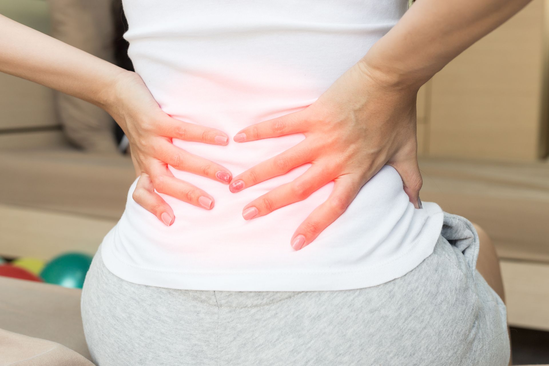 Woman holding her lower back in pain, with red highlighting.
