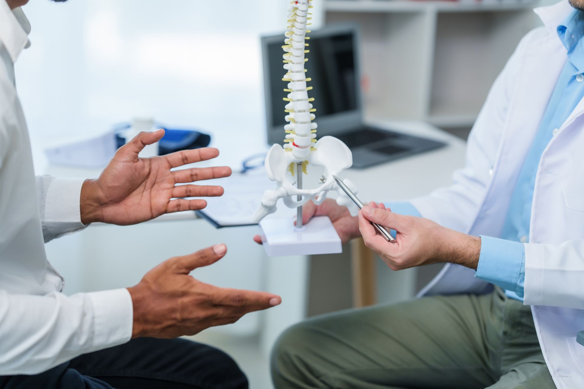 Doctor pointing at spine model, explaining to a patient in an office.