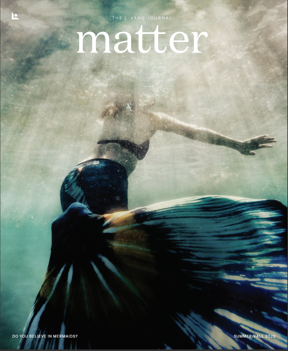 An underwater figure with a prominent, dark-patterned tail swims upward through sunlit, textured blue water.