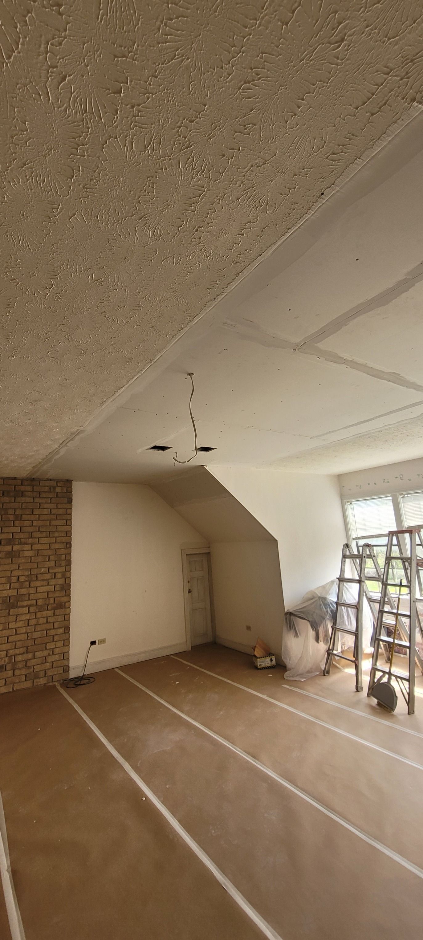 Interior of a room under construction with exposed ceiling, bare floors, and a brick wall.