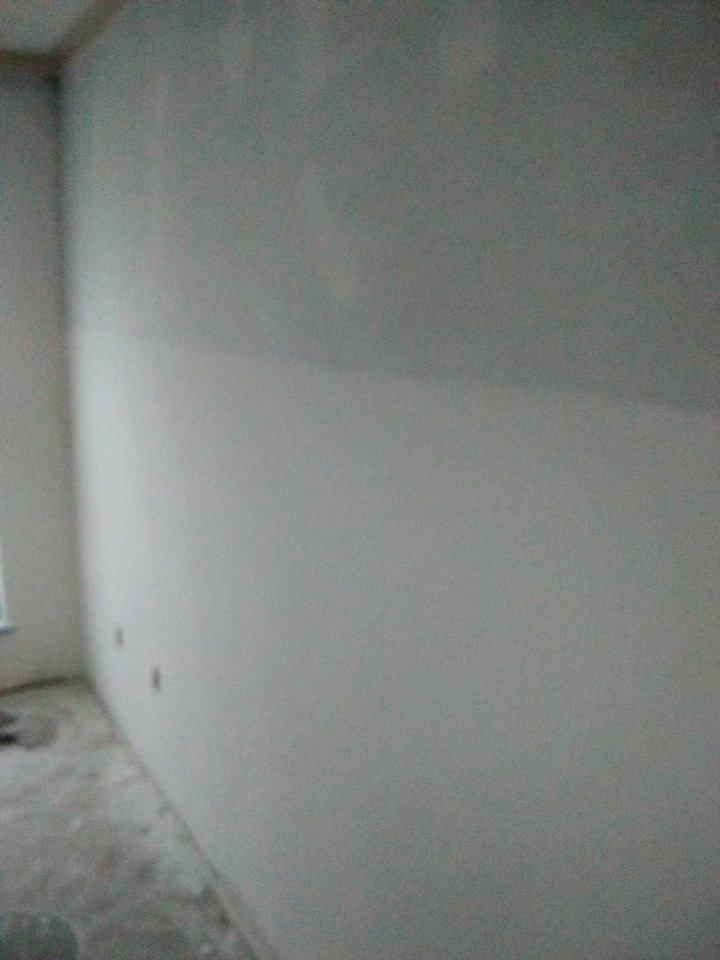 Light gray interior wall with electrical outlets, freshly plastered.  A portion of the wall has a darker gray tint.
