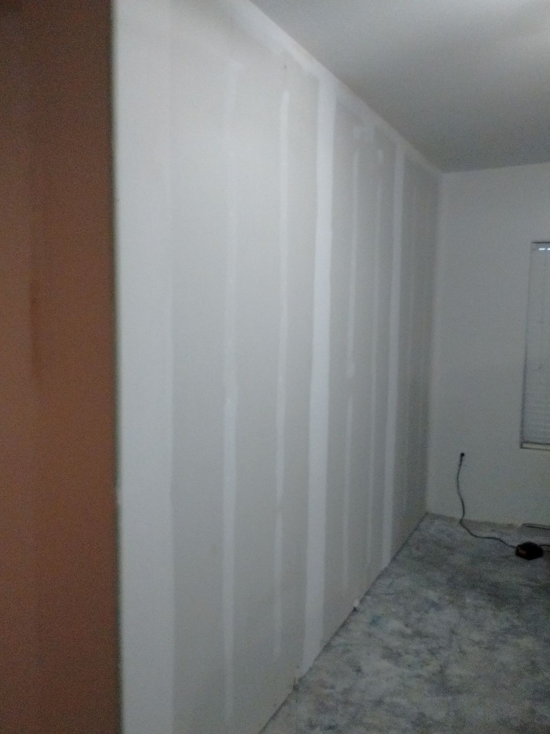 White drywall wall with vertical seams, next to a tan door and a room with a window.