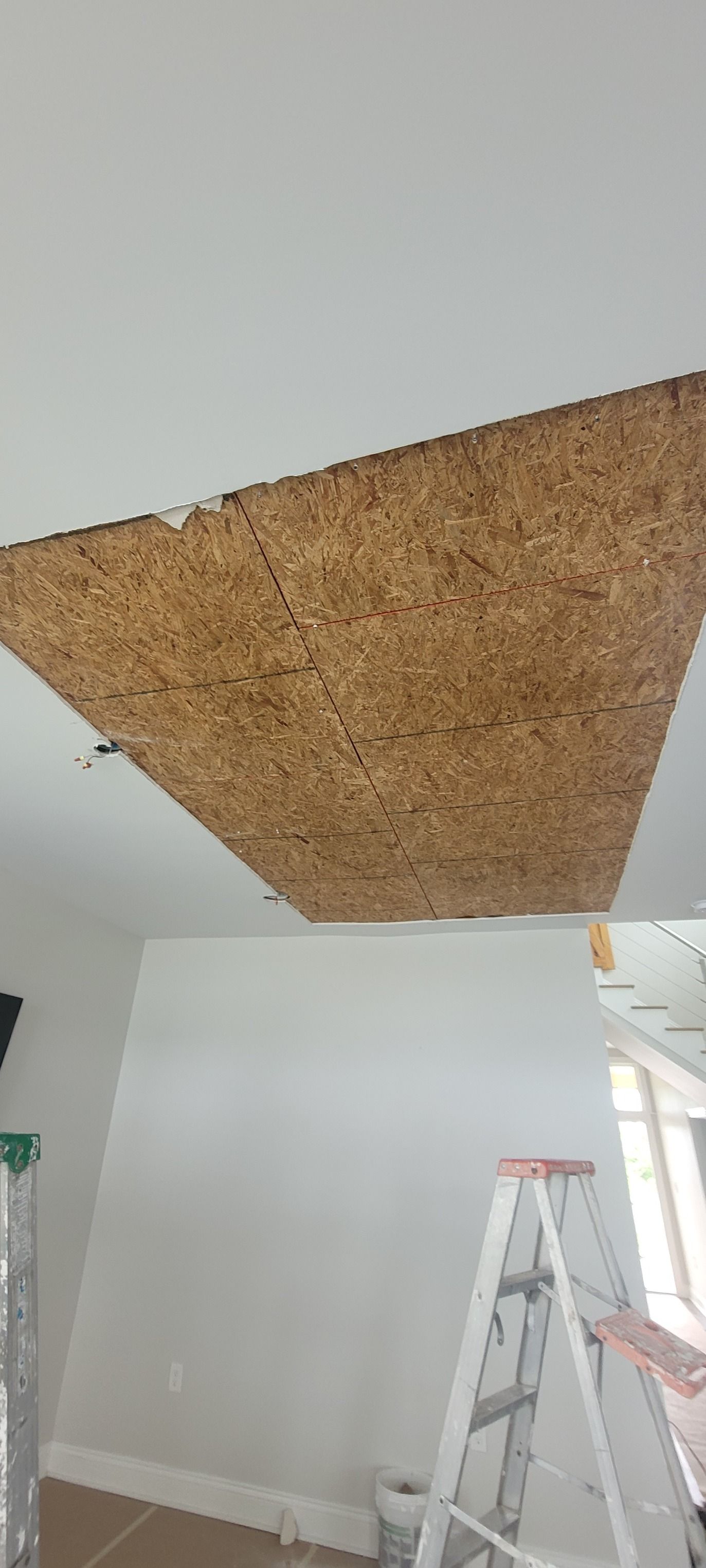 A damaged ceiling exposes the construction material. Ladders and a white wall are in the room.