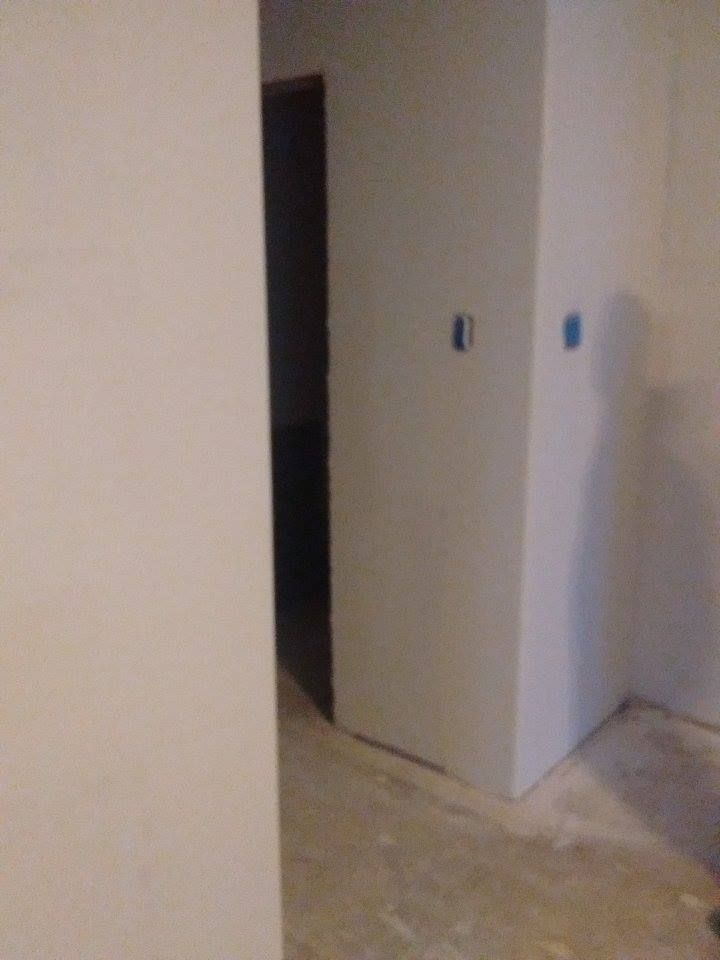 A doorway leads down a dark hallway, flanked by off-white walls with blue electrical boxes. The floor is bare concrete.