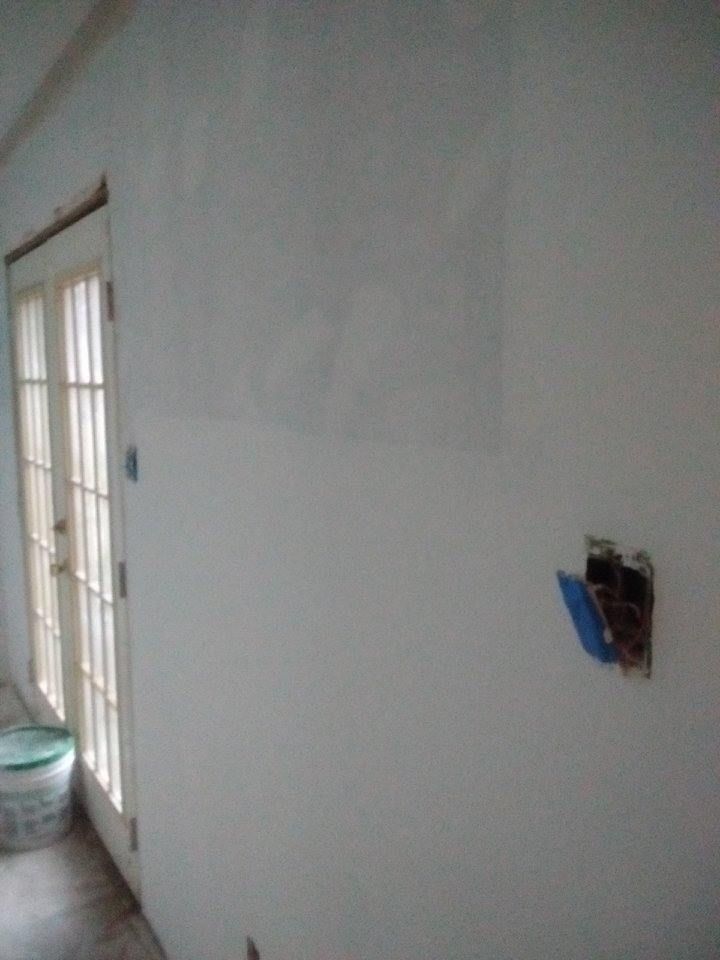 White wall with a door on the left and an electrical outlet on the right. A bucket sits on the floor near the door.