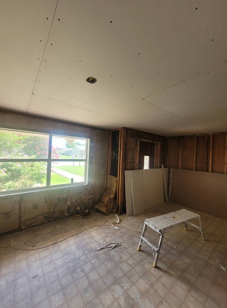 A room under renovation with exposed framing and drywall. A window offers a view outside. A step stool sits in the center.