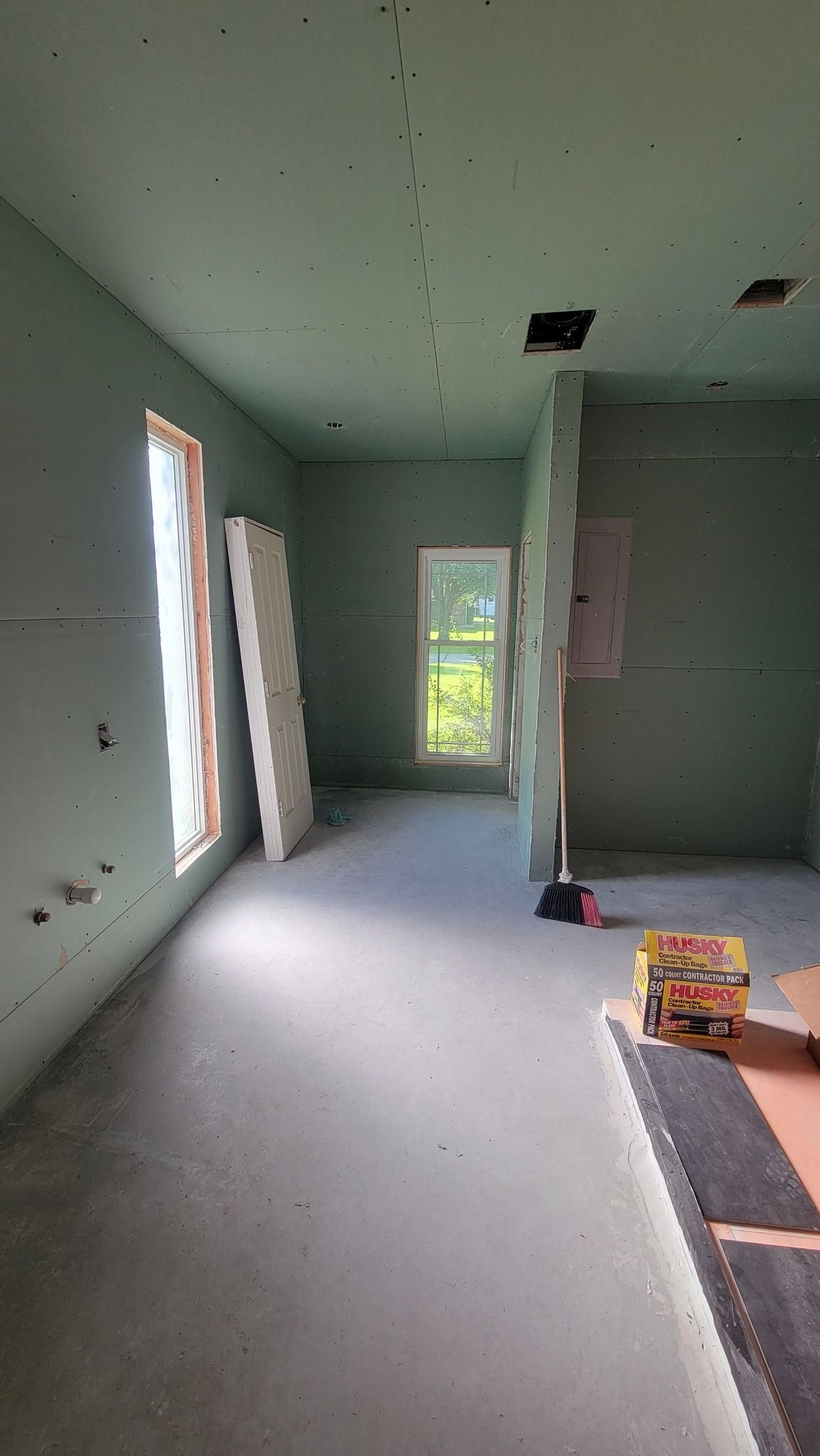 Interior of a room under construction with drywall installed. Windows let in natural light.