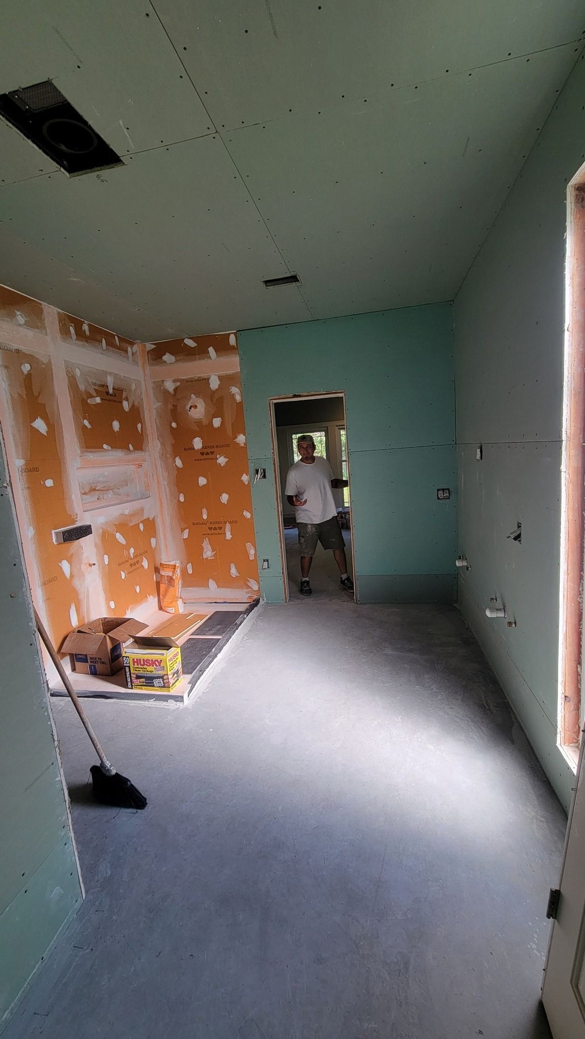 Room under construction with green drywall, orange shower backer board, and a person standing in a doorway.