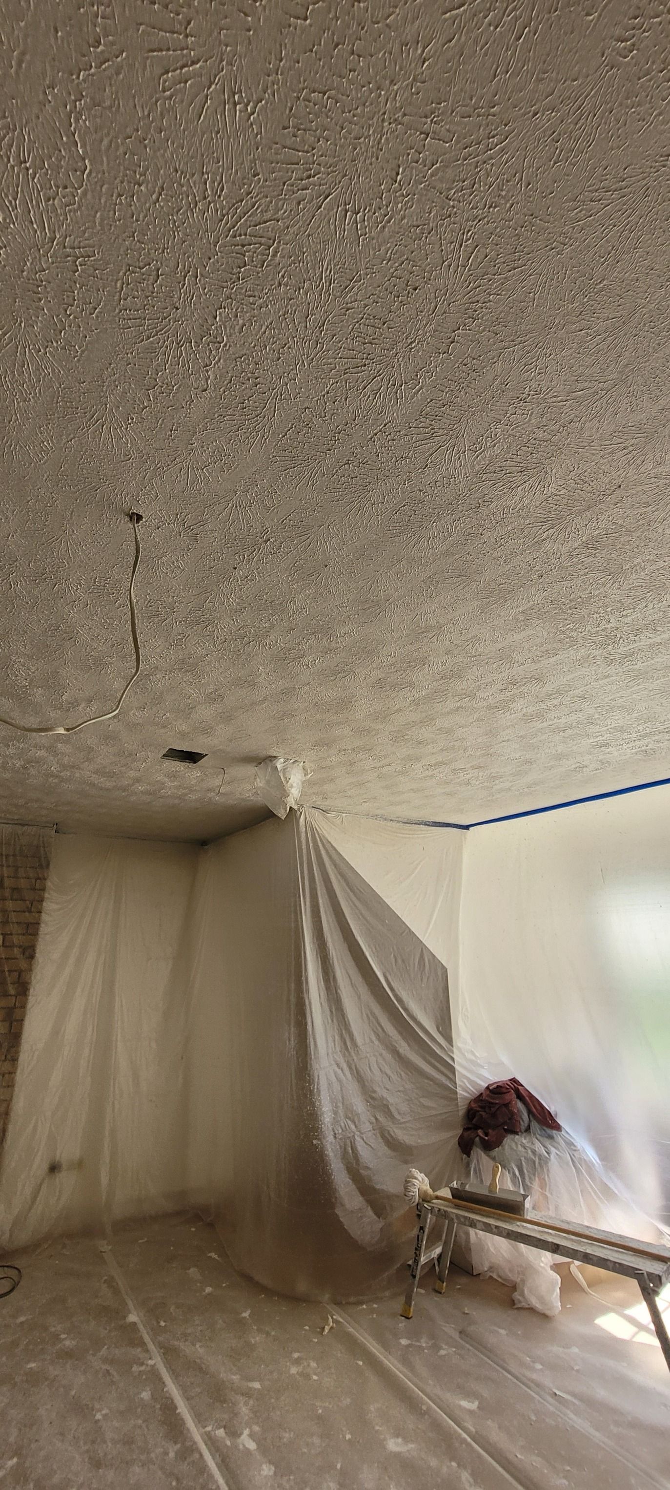 A room with popcorn ceiling covered in plastic for renovation. The floor is also covered, with a white wall on the right.