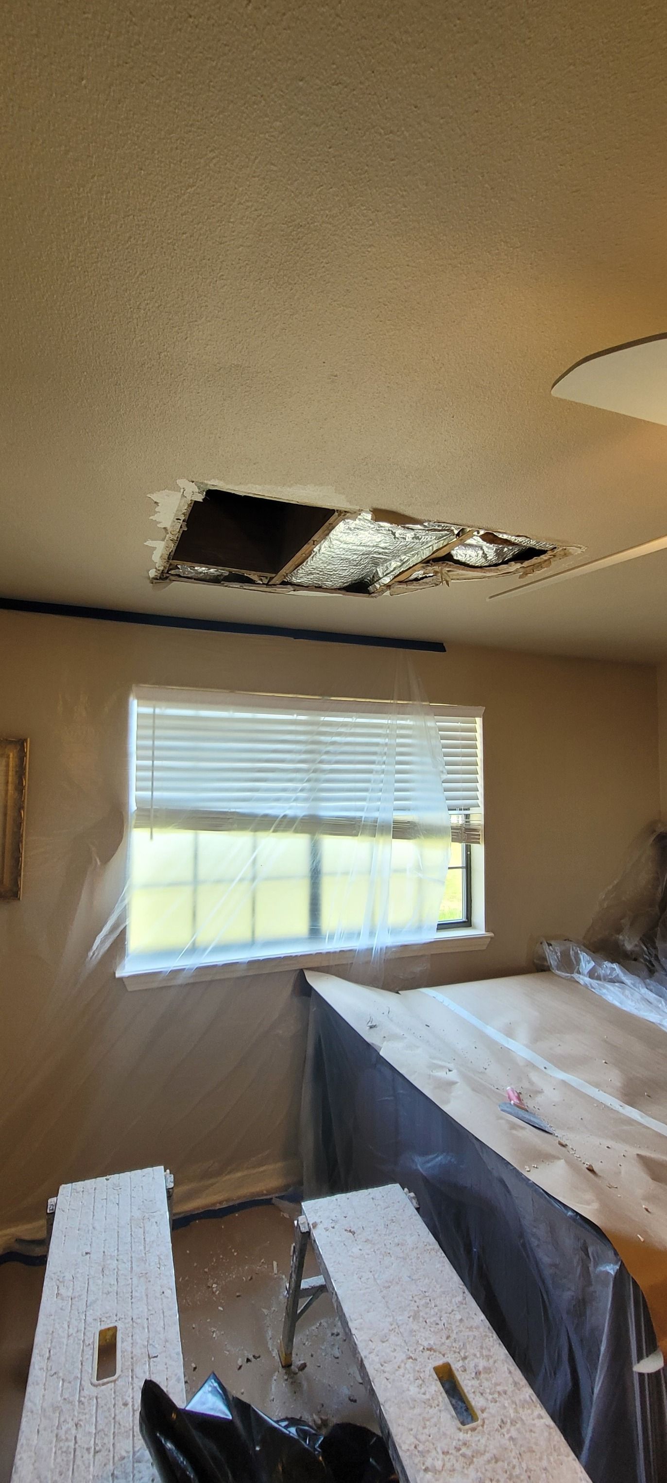 A room with a hole in the ceiling, likely from a leak. Blinds on the window, and work supplies on the floor.
