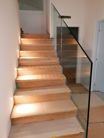 Scala in legno in costruzione con ringhiera in vetro all'interno di un'abitazione luminosa.