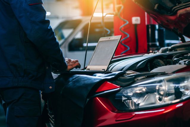 A mechanic is using a laptop computer to check the engine of a car.