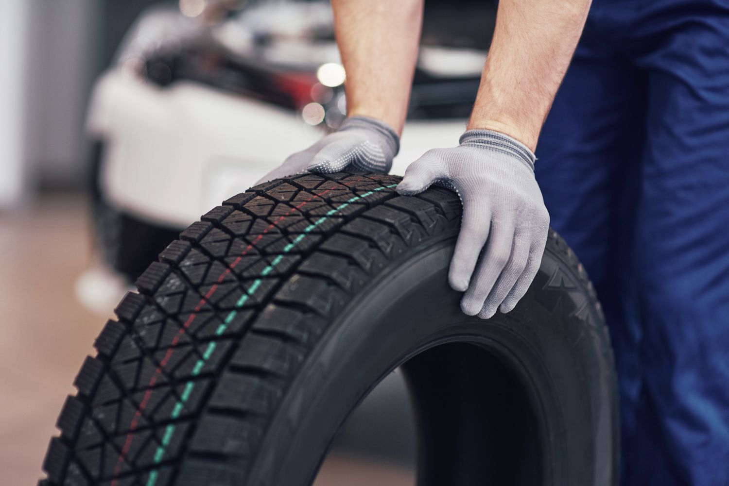 A man is holding a tire in his hands in front of a car.