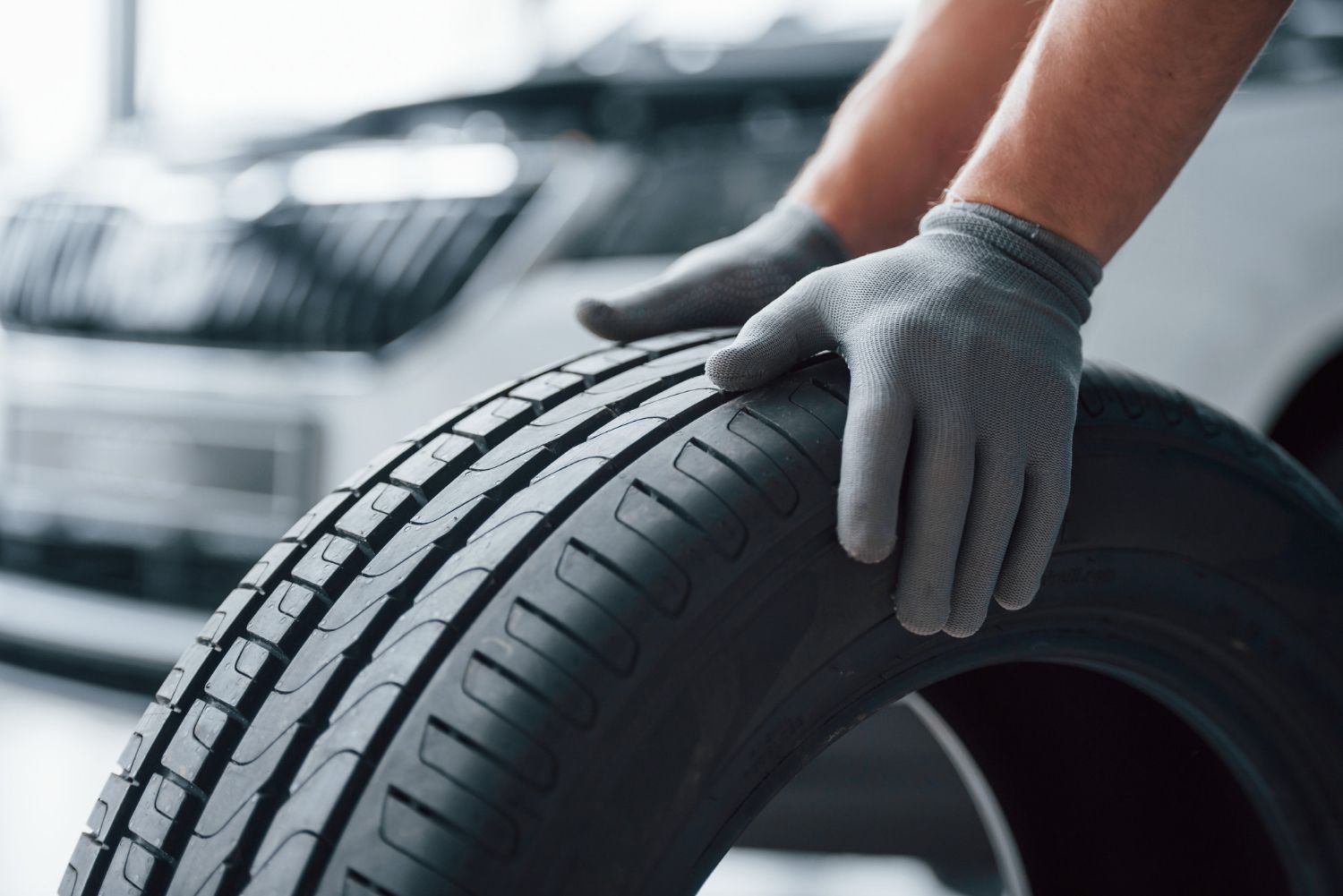 A person wearing gloves is holding a tire in front of a car.