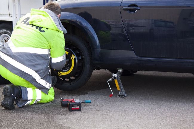 A man in a yellow jacket is changing a tire on a black car.