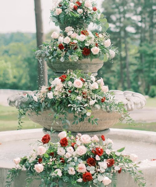 Flower-covered white fountain in a garden, decorated with white and red roses.