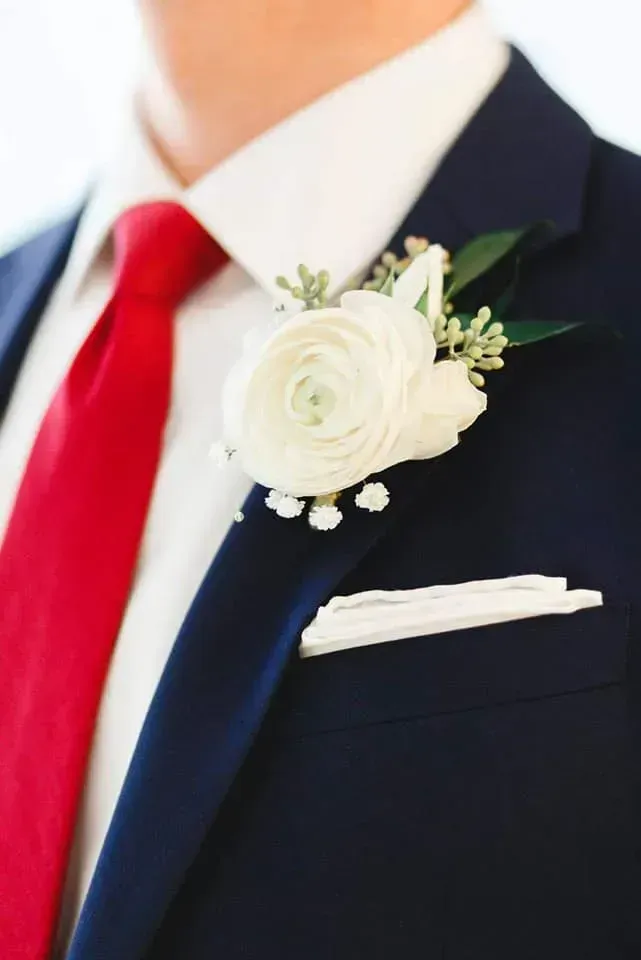 Dark suit with red tie and white boutonniere on lapel, close-up at a wedding.