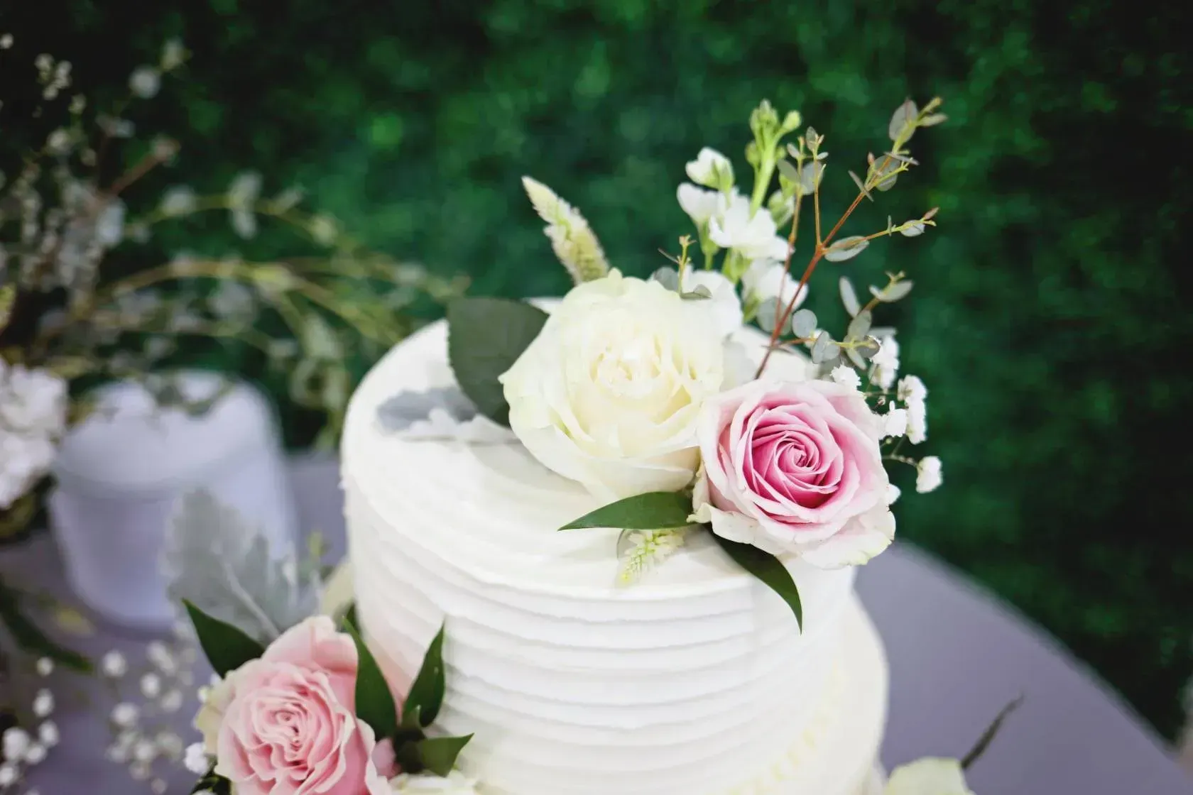 White wedding cake topped with white and pink roses on a table outdoors