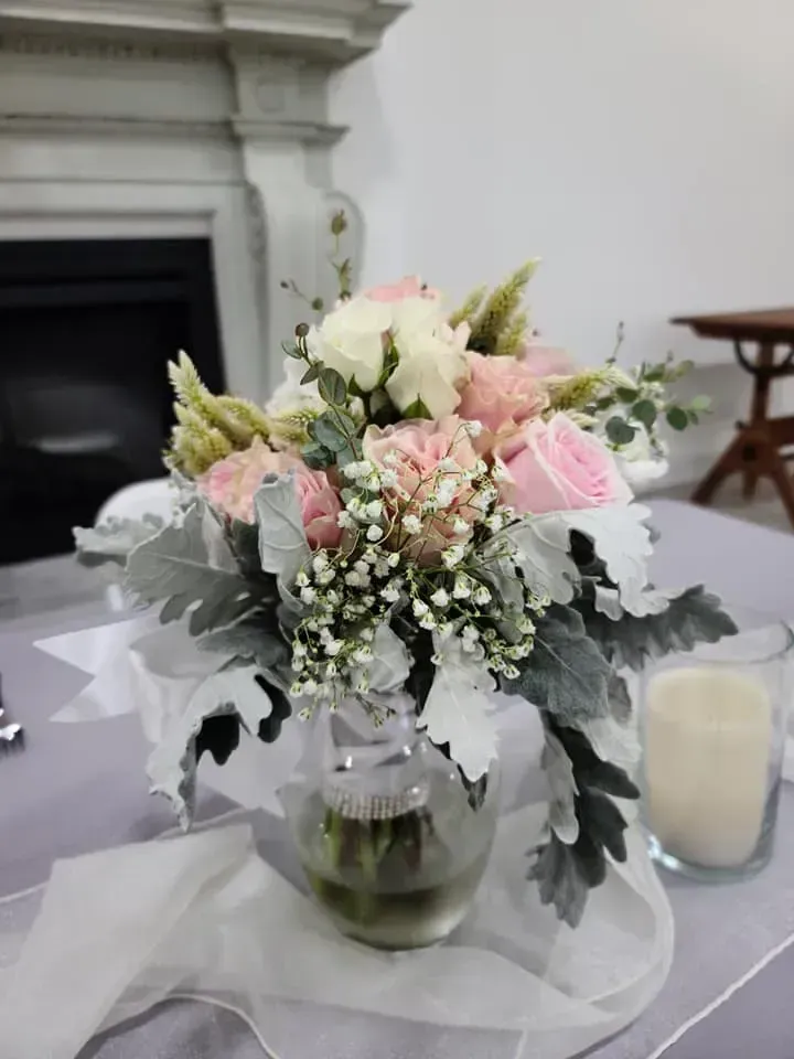 Pink and white floral arrangement in a glass vase on a table with candles