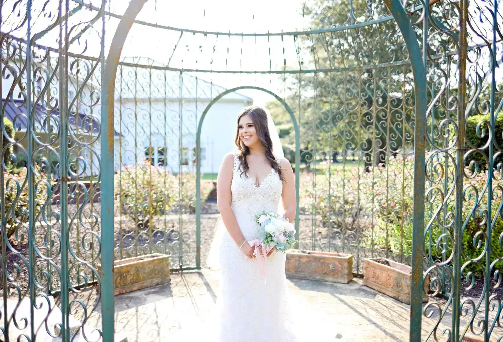 Bride in a white dress holding a bouquet under a garden archway outdoors