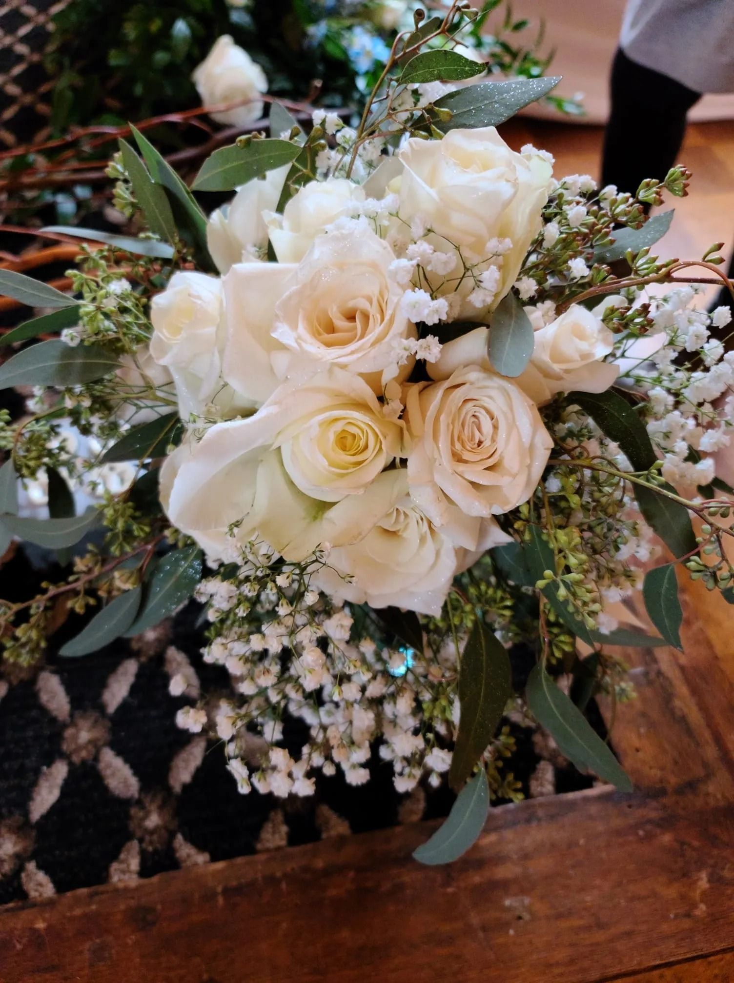 White rose bouquet with greenery and baby's breath on a wooden surface