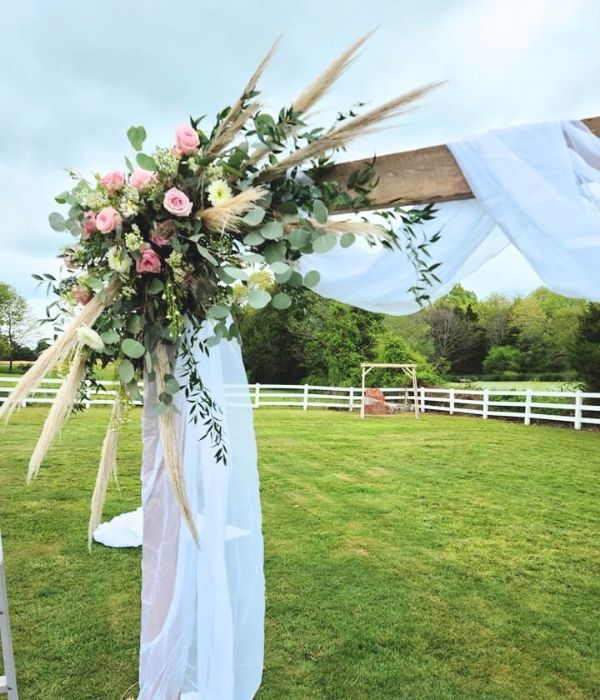 Floral wedding arch with white drapery on a green lawn under a blue sky