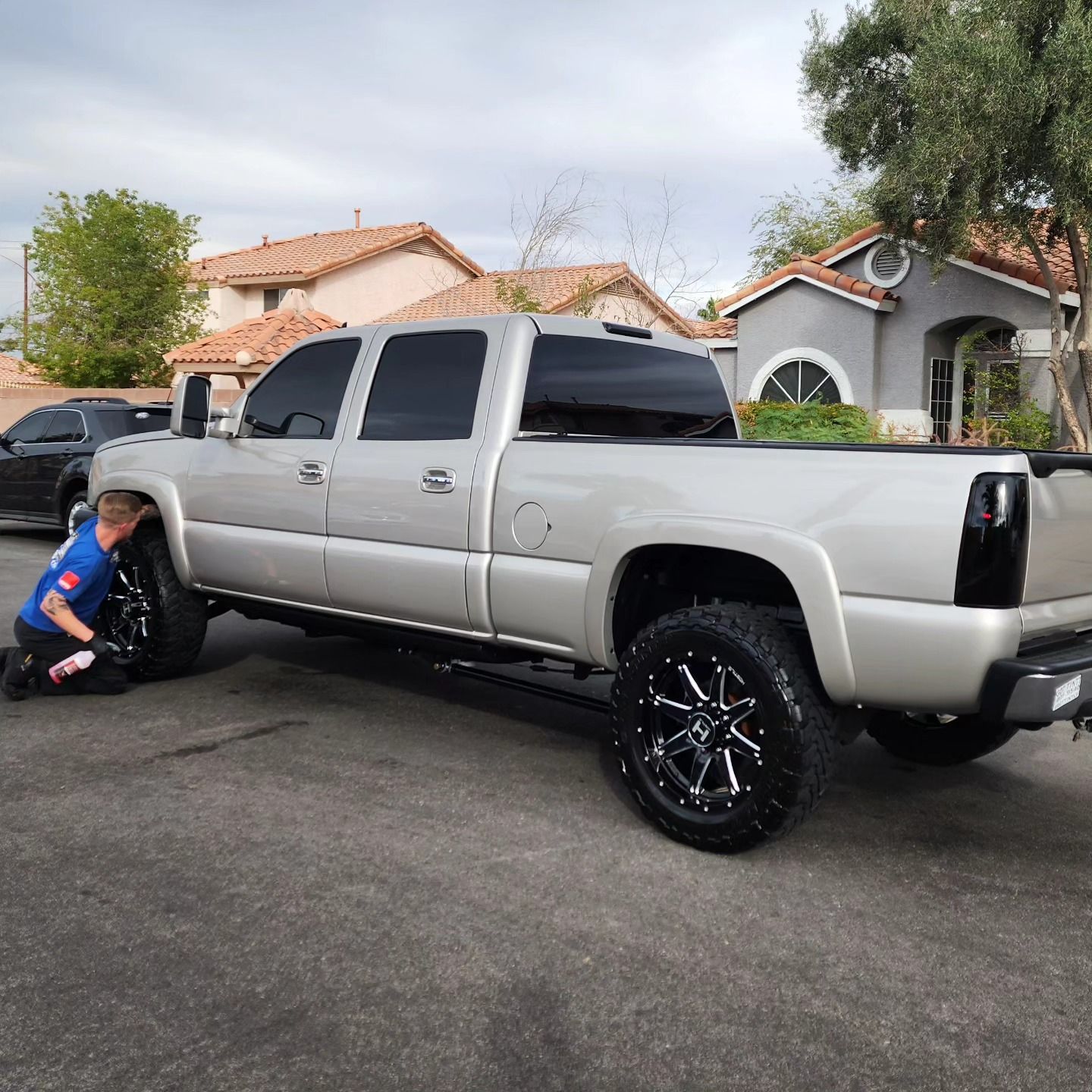 A man is kneeling next to a silver truck in a parking lot