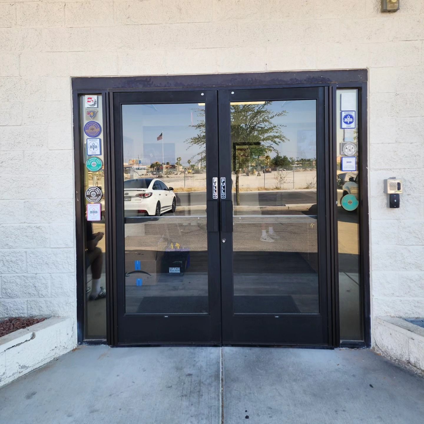 A white car is reflected in the glass doors of a building
