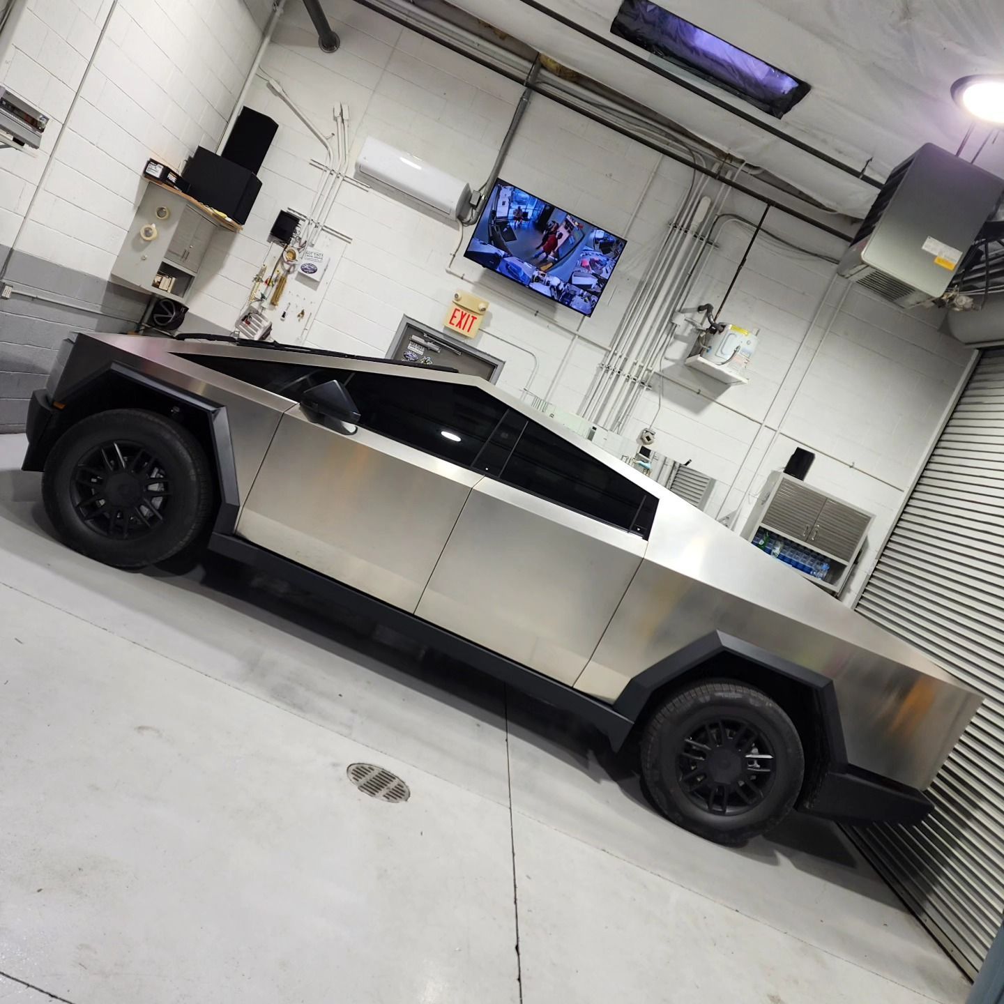 A silver car is parked in a garage with a tv on the wall.