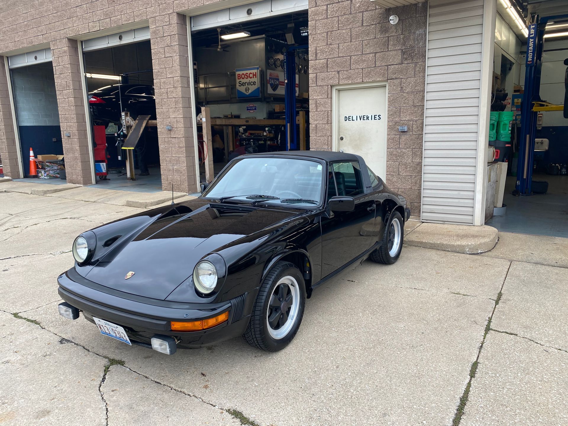Black classic Porsche sports car parked outside an auto repair garage