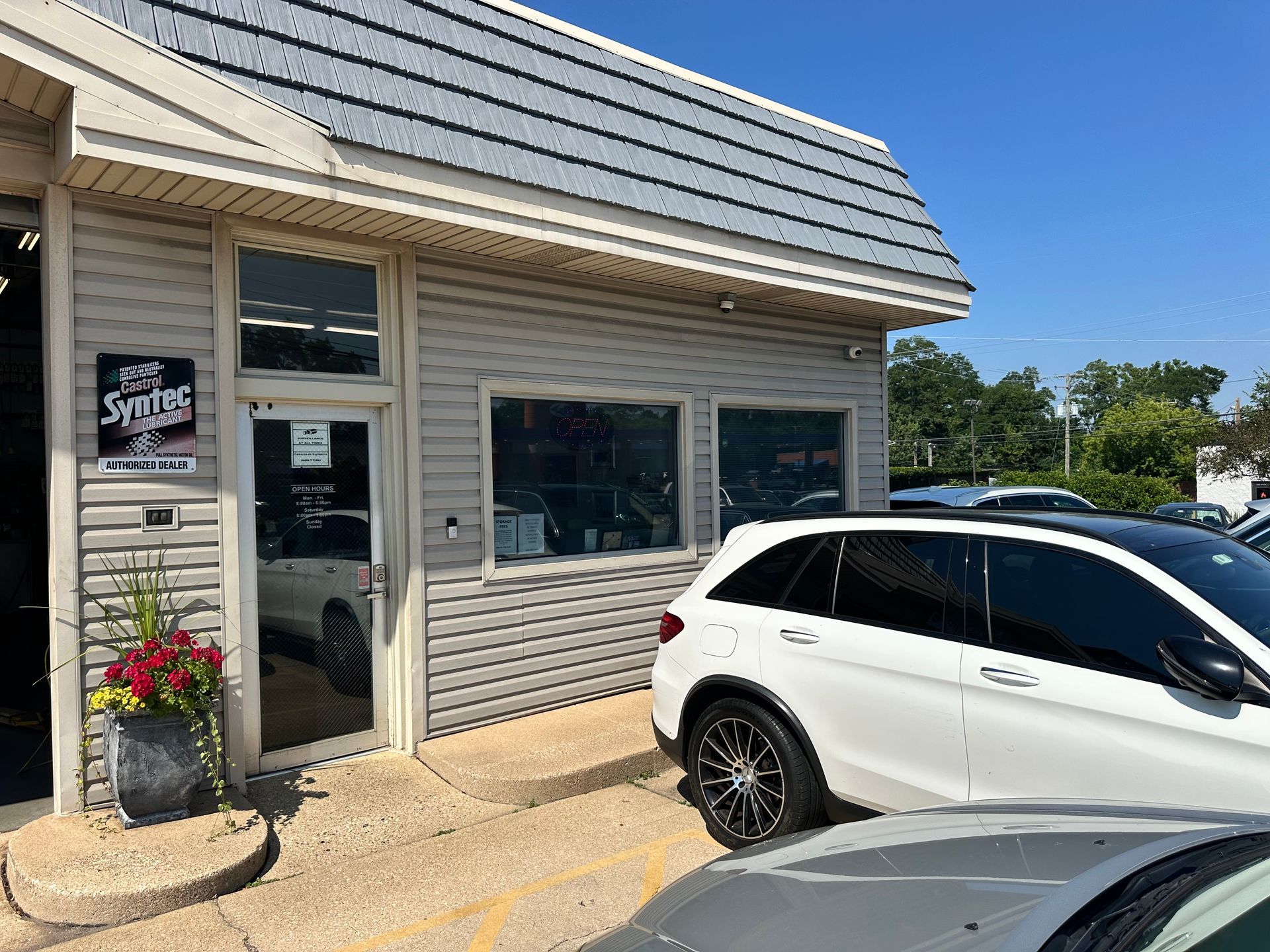 Small storefront with gray siding and a white SUV parked in front on a sunny day