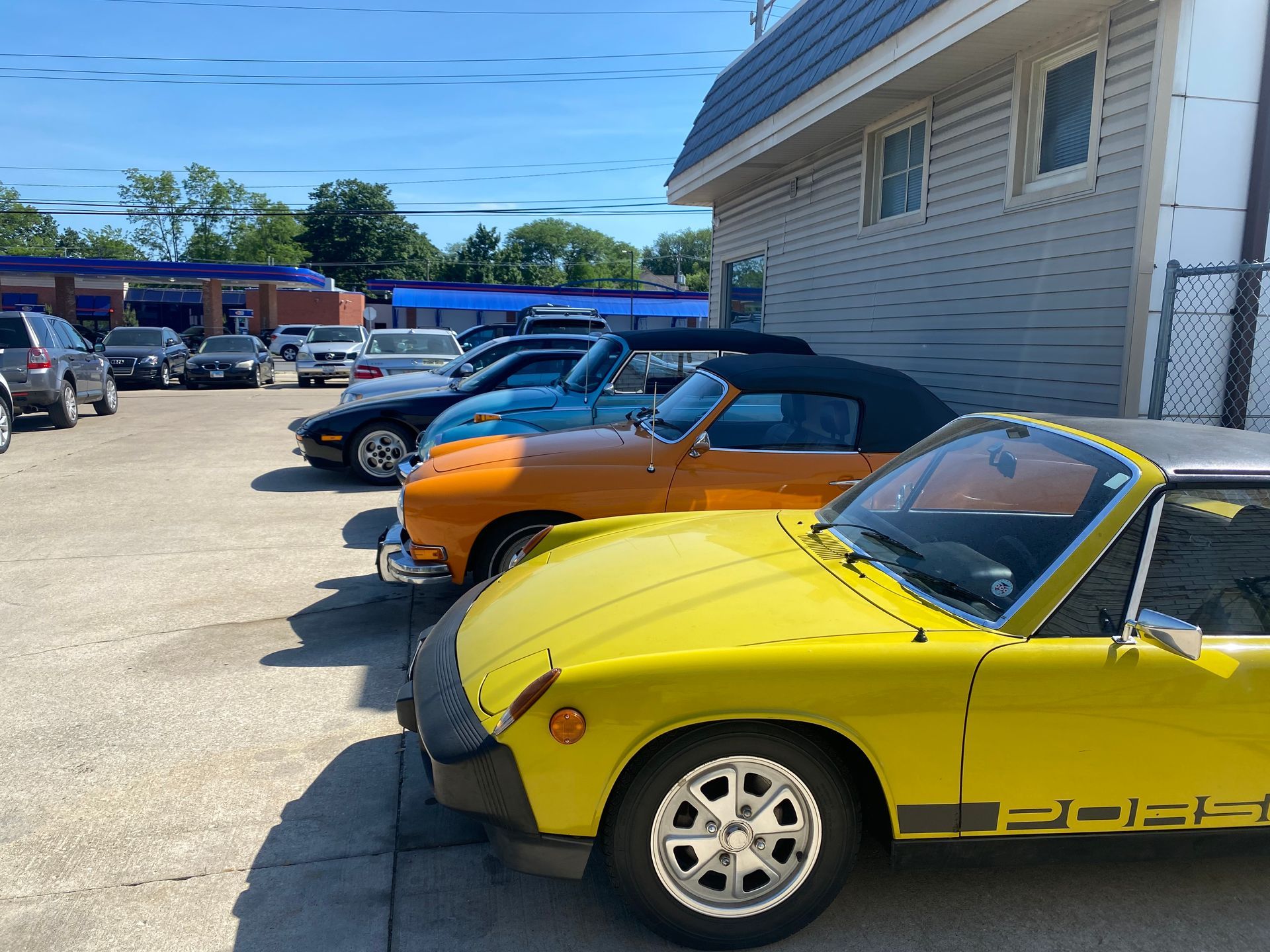 Yellow classic convertible parked beside orange and black sports cars by a building on a sunny day