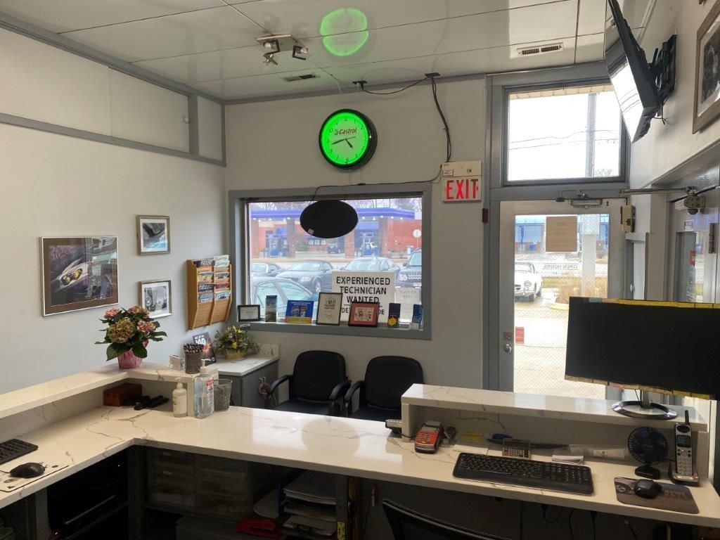 Small office reception desk with computer monitors, wall clock, window, and lobby chairs.