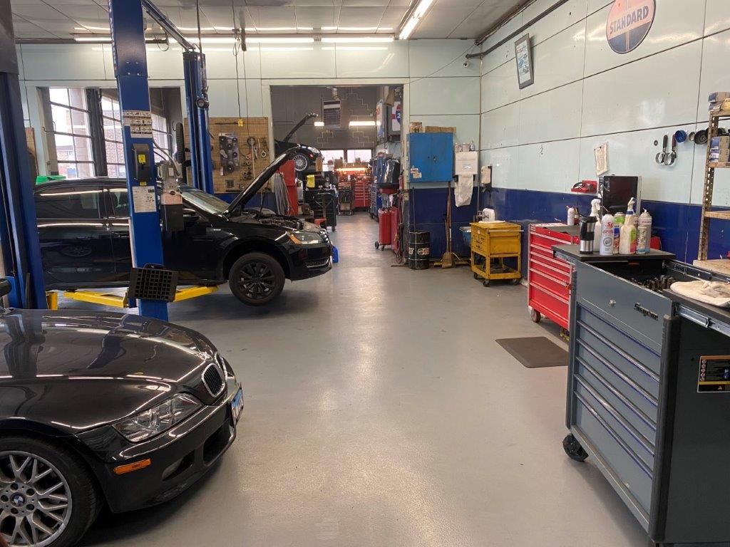Auto repair shop with a lifted Jeep, black car, and tool cabinets inside a garage