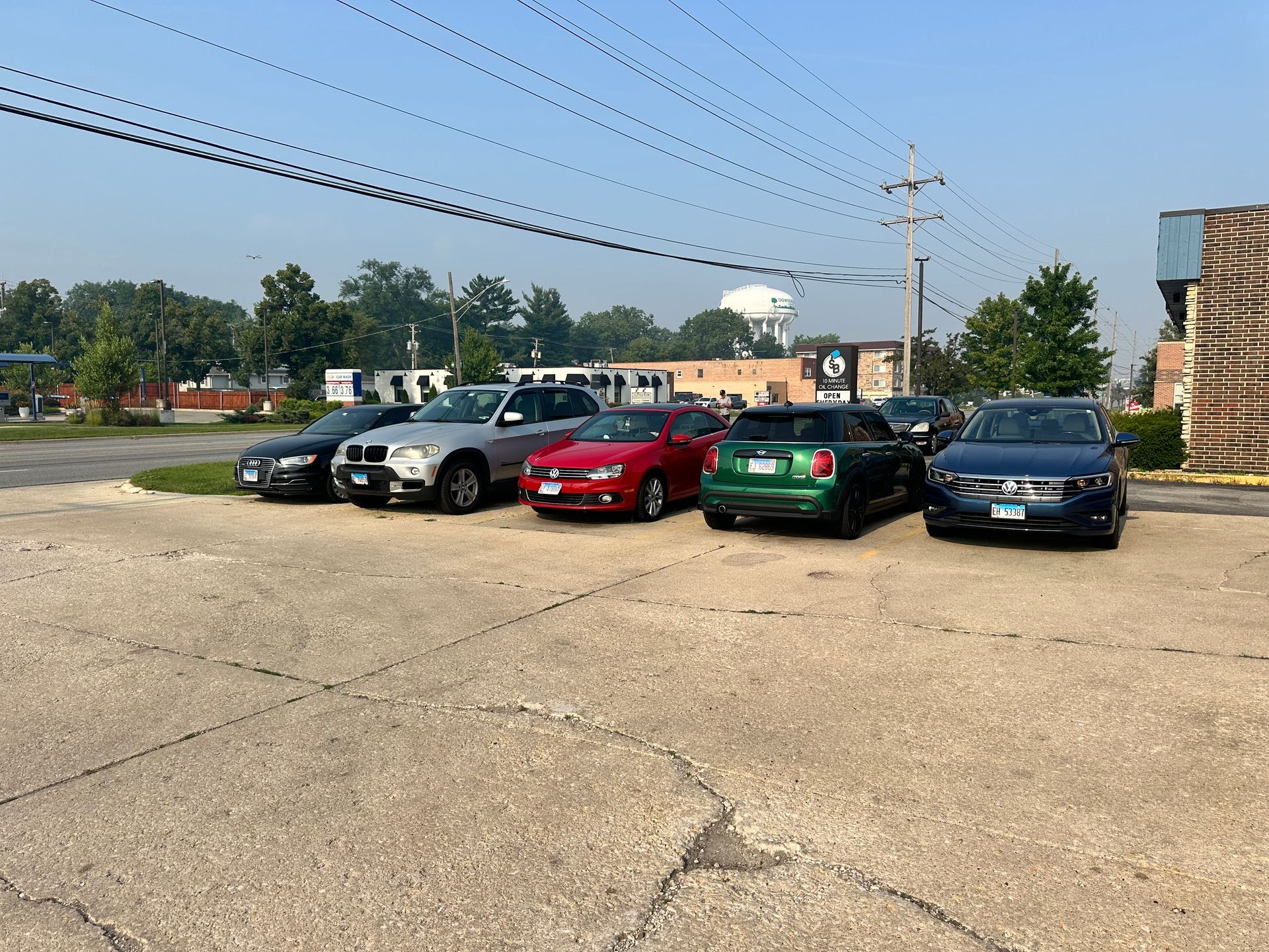 Five parked cars in a lot beside a brick building under a clear sky