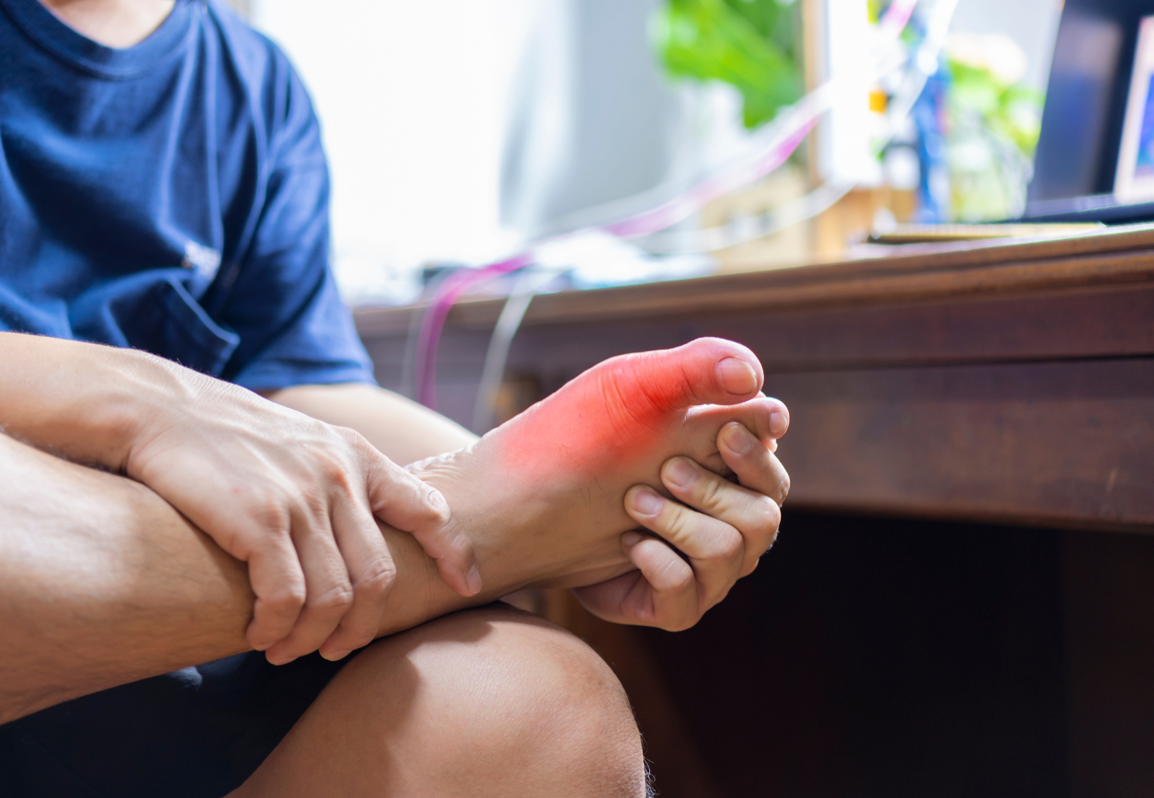 A man is sitting at a desk holding his foot in pain.