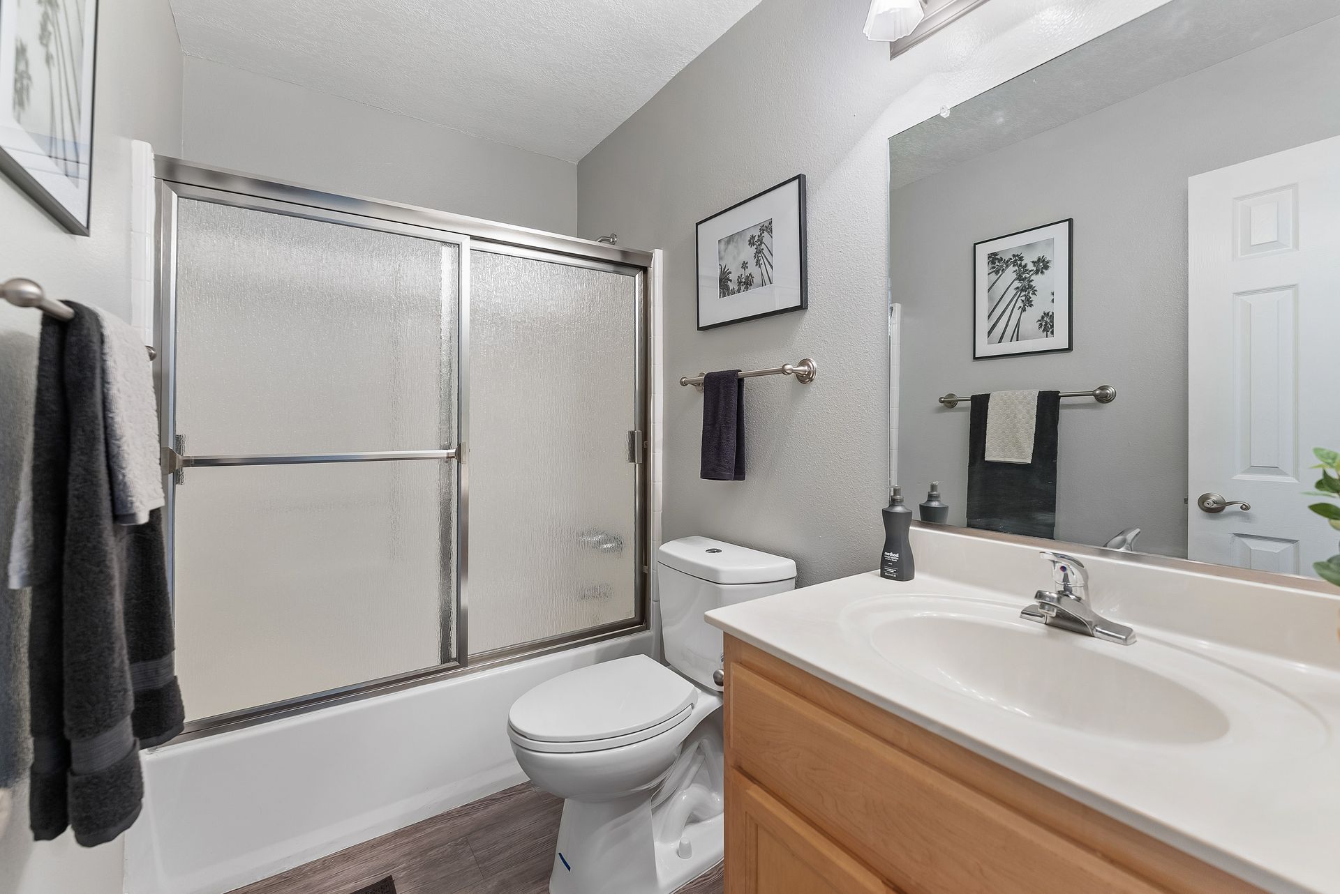 Bathroom with maple wood cabinets, black towels, and shower