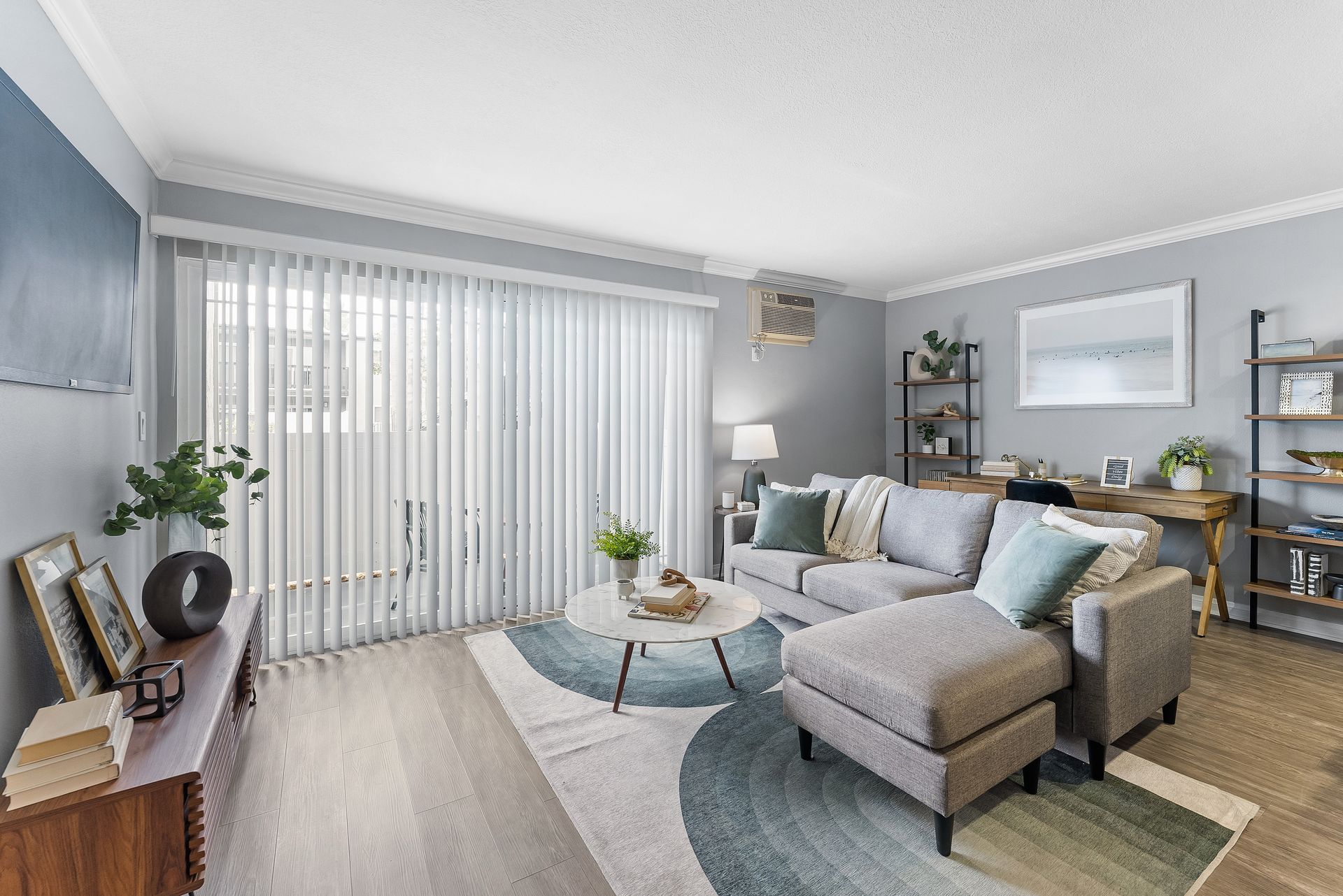 Interior living room with wood floors, white coffee table, and grey couch with pillows with patio window